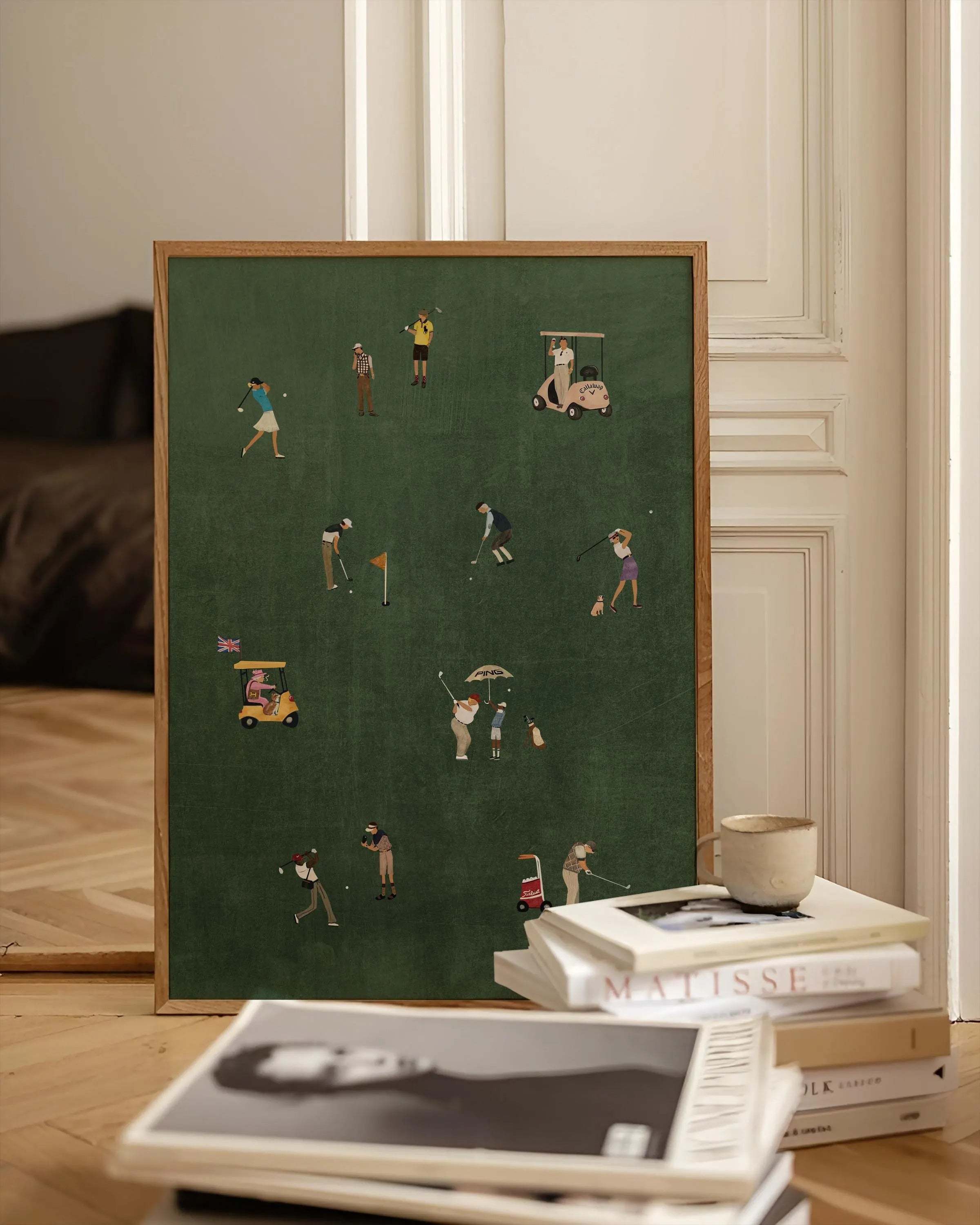 Framed artwork of golfers on a green background, displayed on a table with books.