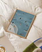 Golden Days framed beach and swimming print resting on white bedding.