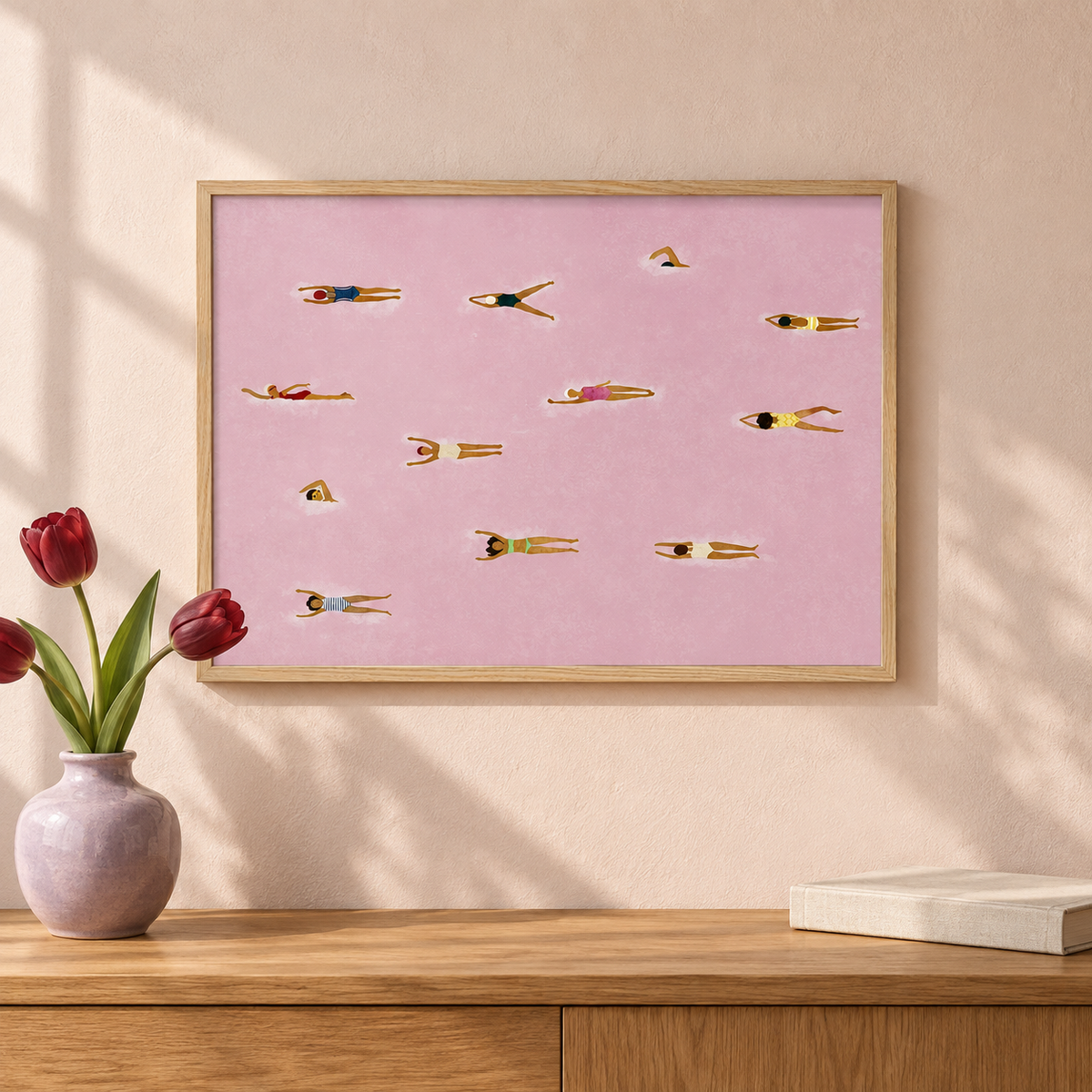 The Red Sea pink swimmers print styled above an oak console with tulips; lifestyle visualisation.
