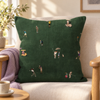 Tiny Golfers dark green pillow styled on a cream armchair with a lavender throw; lifestyle visualisation.