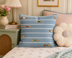 Blue swimming lanes Beach Day Pillow on floral bedding beside a pink lamp.